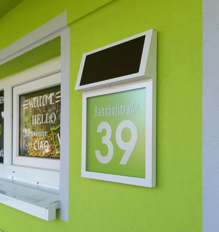 Solar-Hausnummer mit weißem Gehäuse und hellgrünem Hintergrund an einer hellgrünen Wand.