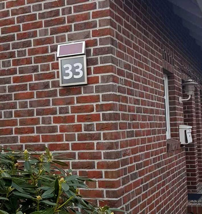 Solarhausnummer aus Edelstahl mit grauem Hintergrund und Nummer 33 an einer Klinkerfassade.