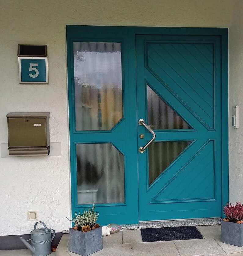 Solarhausnummer in Edelstahl mit Hintergrund in türkis neben einer türkisen Tür.